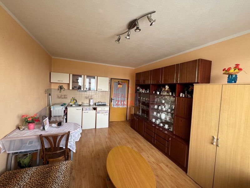 Na predaj Garsônka, 24,5 m2, s perfektnou polohou.  - Garsónka s kuchyňou, obývacou stenou, stolom a podlahou s dreveným dekorom.