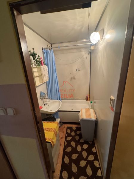 Na predaj Garsônka, 24,5 m2, s perfektnou polohou.  - Kúpeľňa v garsónke s vaňou, umývadlom a modrým závesom.