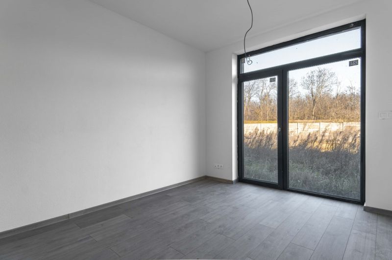 Na predaj nový moderný 4-izbový rodinný dom s terasou a záhradou - Izba v rodinnom dome s veľkým oknom a podlahou s dreveným dekorom.