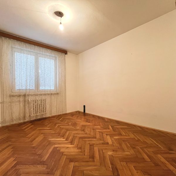 3-izbový byt s veľkou loggiou - Prázdna izba v 3-izbovom byte s podlahou s dreveným dekorom a závesom na okne.