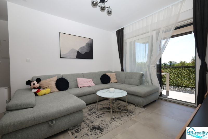 Chorvátsko, Vodice - zariadený apartmán s výhľadom na more - Obývačka v Rekreačnom apartmáne s pohodlnou sivou pohovkou a výhľadom na terasu.