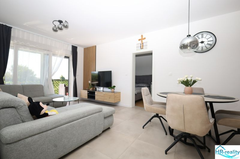 Chorvátsko, Vodice - zariadený apartmán s výhľadom na more - Obývačka rekreačného apartmánu so svetlou pohovkou, jedálenským stolom a televízorom.
