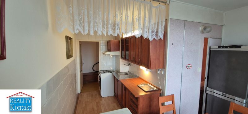 Na predaj 2 izbový byt 62m2 s 3 balkónmi - Nové Zámky  - Kuchyňa v 2-izbovom byte s podlahou s dreveným dekorom a záclonami.