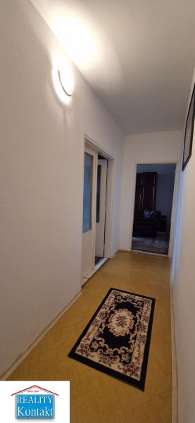 Na predaj 2 izbový byt 62m2 s 3 balkónmi - Nové Zámky  - Chodba 2-izbového bytu so svetlým kobercom a podlahou s dreveným dekorom.