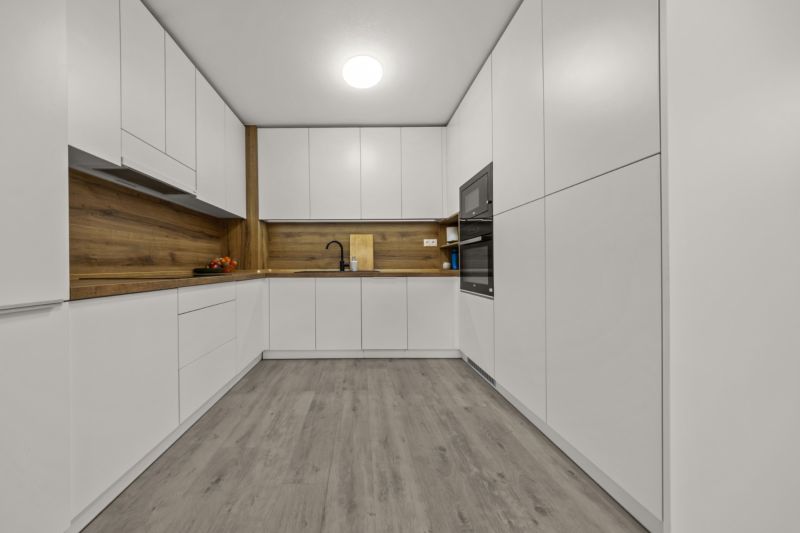 NA PREDAJ: 3-izbový apartmán, MATADORKA, Bratislava - Petržalka - Kuchyňa v 3-izbovom byte s bielymi skrinkami a podlahou s dreveným dekorom.