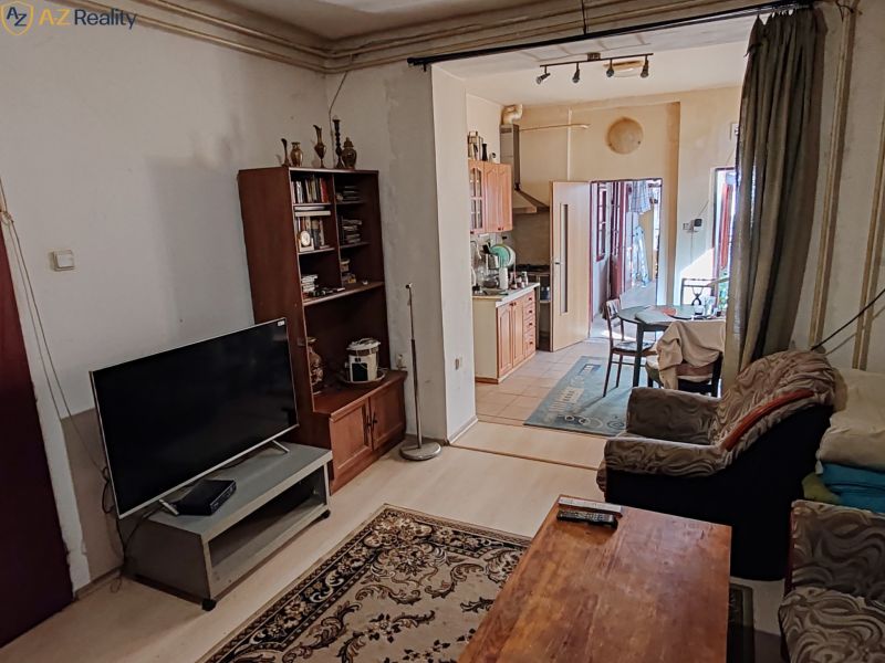 Rodinný dom na predaj Komárno - Obývačka so sedačkou, TV a poličkou, otvorené prepojenie s kuchyňou a jedálenským kútom.