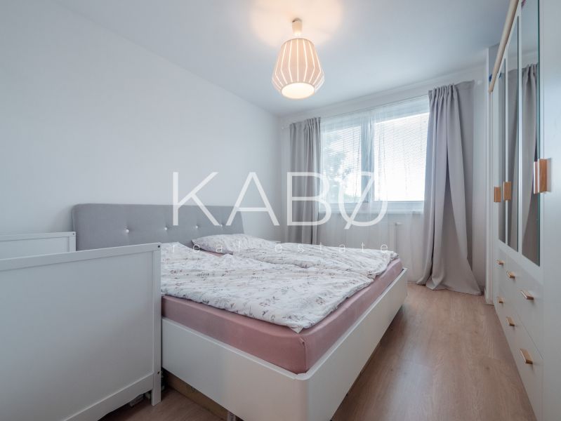 Zariadený- Nízke náklady- Novostavba - Spálňa v 3-izbovom byte s posteľou, skriňou a podlahou s dreveným dekorom.