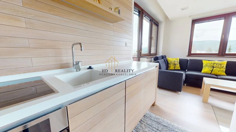 Pripravujeme do ponuky jedinečný apartmánový bytový dom Donovaly  - Interiér chaty s kuchynskou linkou, pohovkou a podlahou s dreveným dekorom.