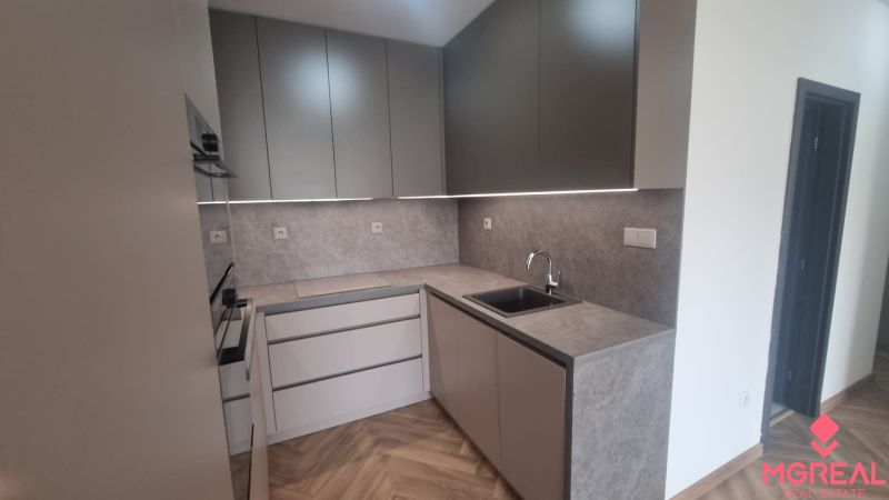 2-izbový moderný byt, s garážovým státím  novostavba, Coboriho ulica - Kuchyňa s podlahou s dreveným dekorom v 2-izbovom byte, sivé skrinky, vstavaná rúra.