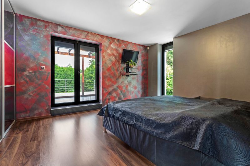 ARCHITEKTÚRA TICHA A MODERNÝCH TECHNOLÓGIÍ - SMART VILLA V OBJATÍ LESA - Spálňa v rodinnom dome s posteľou, farebnými stenami a podlahou s dreveným dekorom.