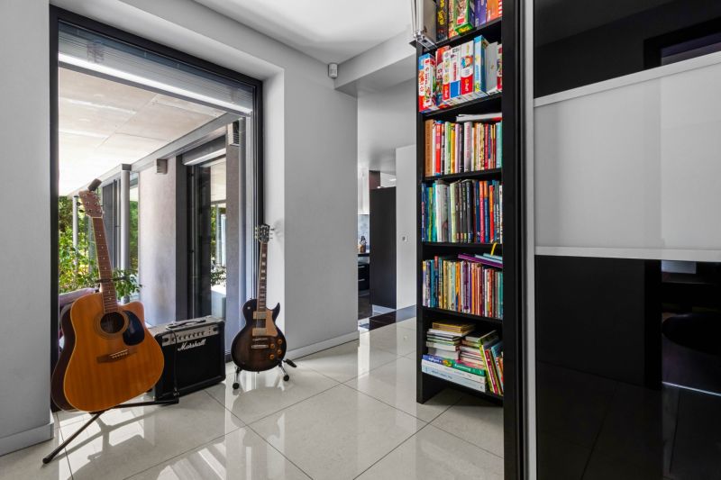 ARCHITEKTÚRA TICHA A MODERNÝCH TECHNOLÓGIÍ - SMART VILLA V OBJATÍ LESA - Interiér rodinného domu, knihy, dve gitary a zosilňovač na podlahe s dlažbou.