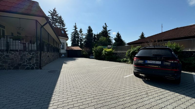 NA PREDAJ hotel s reštauráciou - Parkovisko pre hotely a penzióny s autom, stromami a budovou v pozadí.
