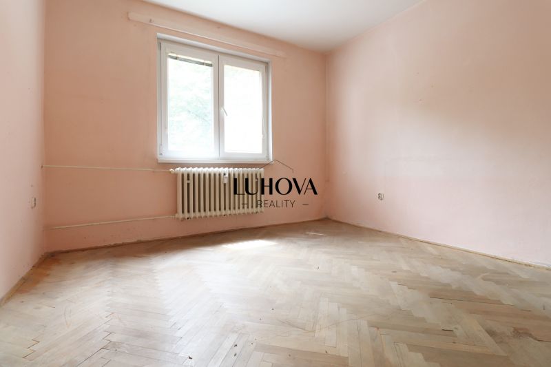 Pôvodný stav, neobmedzené možnosti | 3-izbový byt v centre Púchova  - Izba s radiátorom a podlahou s dreveným dekorom v 3-izbovom byte.