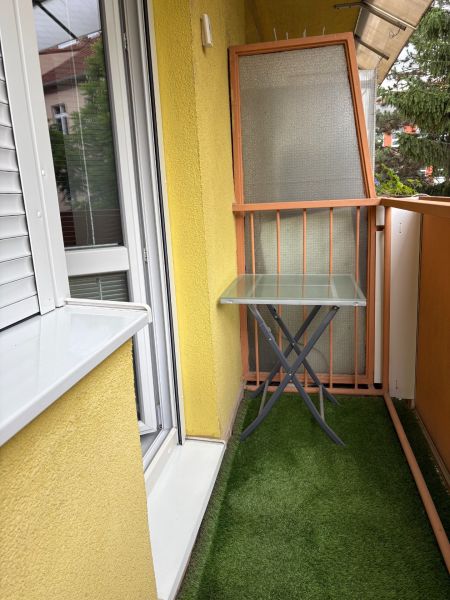 Ponúkame na predaj veľký 2 i byt v Nových Zámkoch, ul. Šafárikova ! - Balkón 2-izbového bytu s posuvnými dverami a skleneným stolíkom, umelý trávnik.