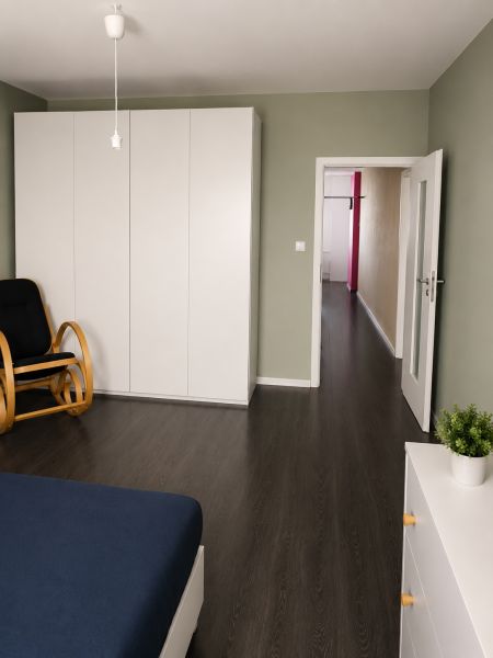 REZERVOVANÝ - Na predaj priestranný 2-izbový byt s balkónom, klímou... - Spálňa s bielou skriňou, dreveným dekorom podlahy a pohodlným kreslom v 2-izbovom byte.
