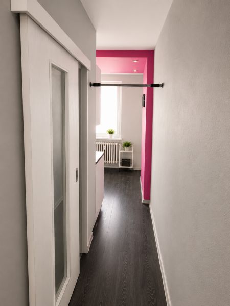 REZERVOVANÝ - Na predaj priestranný 2-izbový byt s balkónom, klímou... - Chodba 2-izbového bytu s posuvnými dverami, podlaha s dreveným dekorom, ružová stena.