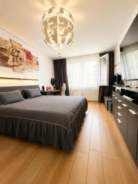 Na predaj Priestranný 2-izbový byt s balkónom v Šali  - Spálňa s posteľou a dekoratívnym osvetlením, 2-izbový byt s podlahou s dreveným dekorom.