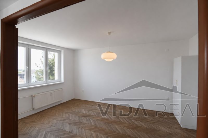 Priestranný 3-izbový byt | 72 m² + 9 m² loggia + 9 m² pivnica |  - Obývacia izba v 3-izbovom byte s podlahou s dreveným dekorom a veľkými oknami.