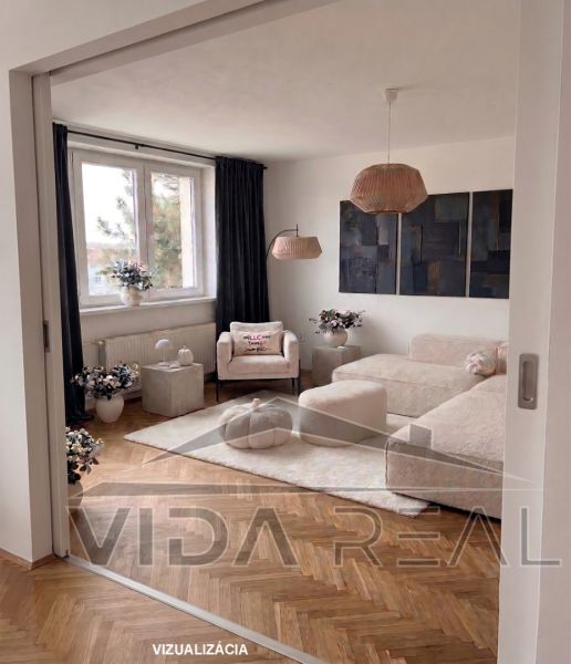 Priestranný 3-izbový byt | 72 m² + 9 m² loggia + 9 m² pivnica |  - Obývacia izba v 3-izbovom byte s pohovkou, kreslom a podlahou s dreveným dekorom.