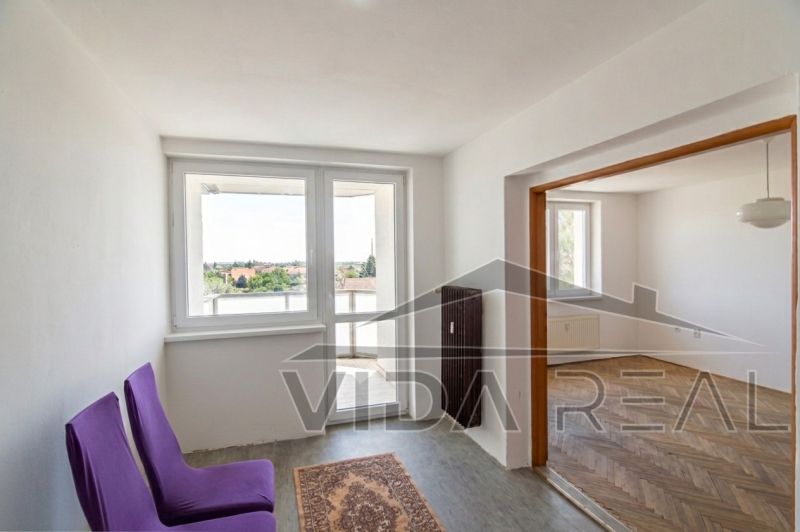 Priestranný 3-izbový byt | 72 m² + 9 m² loggia + 9 m² pivnica |  - Interiér 3-izbového bytu s podlahou s dreveným dekorom, fialovými stoličkami a balkónom.