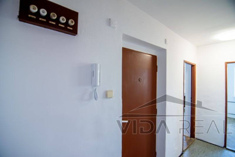 Priestranný 3-izbový byt | 72 m² + 9 m² loggia + 9 m² pivnica |  - Chodba v 3-izbovom byte, biele steny, hnedé dvere, telefón pri vstupe.