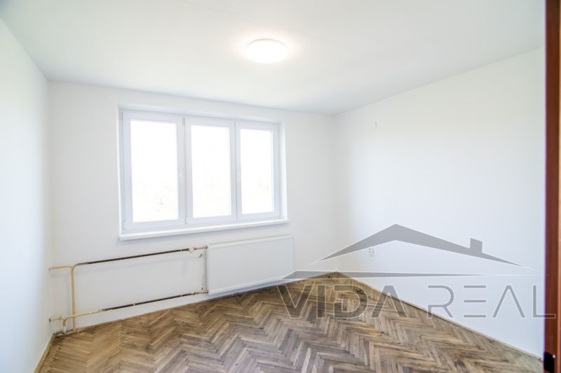 Priestranný 3-izbový byt | 72 m² + 9 m² loggia + 9 m² pivnica |  - Priestor s bielymi stenami, veľkým oknom a podlahou s dreveným dekorom v 3-izbovom byte.
