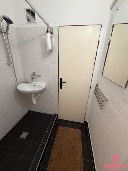 Garsonka Topoľčany / PRENAJOM - Kúpeľňa v garsónke s umývadlom, sprchou a odtokovým žľabom, čierne dlaždice na podlahe.