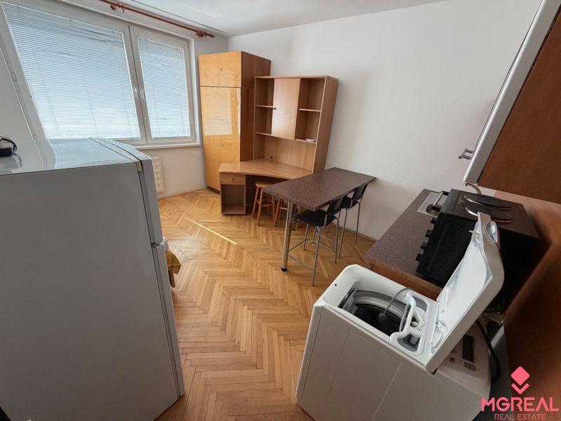 Garsonka Topoľčany / PRENAJOM - Garsónka s podlahou s dreveným dekorom, kuchynským kútom, stolom a práčkou.