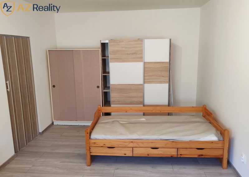 Pekný 1 izbový byt s balkónom na prenájom - 1-izbový byt s posteľou, skriňami a podlahou s dreveným dekorom.