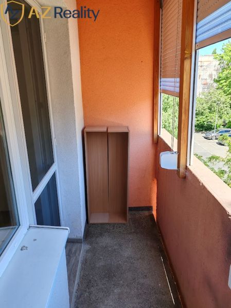 Pekný 1 izbový byt s balkónom na prenájom - Balkón 1-izbového bytu, oranžová stena, drevená skrinka, výhľad na stromy a cestu.