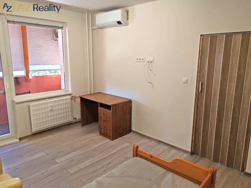 Pekný 1 izbový byt s balkónom na prenájom - 1-izbový byt s podlahou s dreveným dekorom, stolom a radiátorom pri okne.