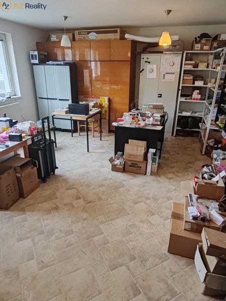 Komerčný objekt na predaj  v Komárne - Miestnosť s kartónmi, kovovými policami, podlaha s dreveným dekorom, stoly s predmetmi.