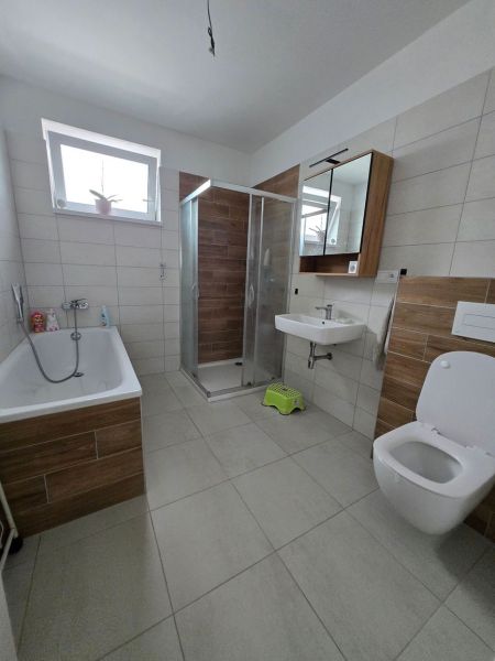 Predaj 4 izbového rodinného domu, pozemok od 523 m2,  NOVOSTAVBA 2023 - Kúpeľňa s vaňou, sprchovacím kútom, zrkadlom a podlahou s dreveným dekorom v rodinnom dome.