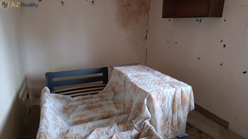 Na predaj starší rodinný dom s podkrovím v obci Gbelce - Izba v rodinnom dome s poškodenými stenami a prikrytou nábytkom.