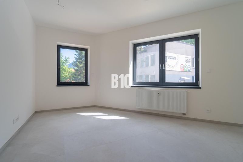 ADMINISTRATÍVNY PRIESTOR (127,87 m²) V NOVOSTAVBE REZIDENCIA KUBÍN V C - Interiér kancelárie s bielymi stenami, sivou podlahou a dvoma oknami.