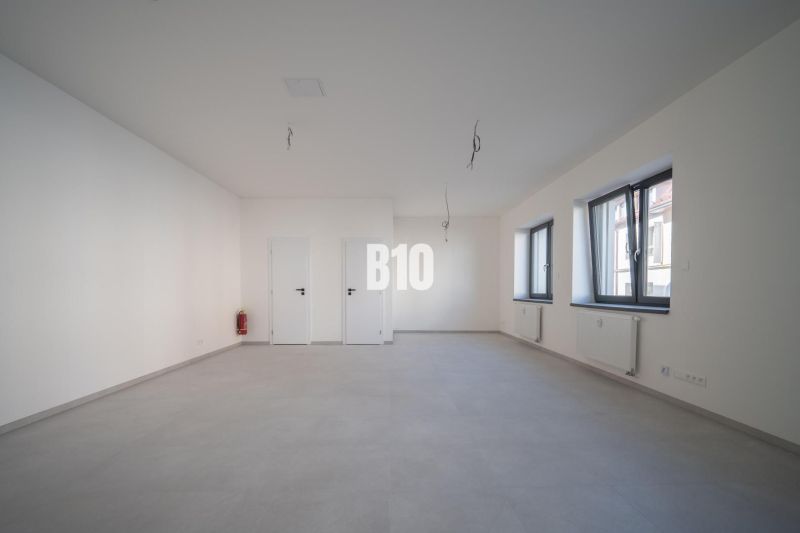 ADMINISTRATÍVNY PRIESTOR (127,87 m²) V NOVOSTAVBE REZIDENCIA KUBÍN V C - Prázdna kancelária s bielymi stenami, šedou podlahou a oknami bez závesov.