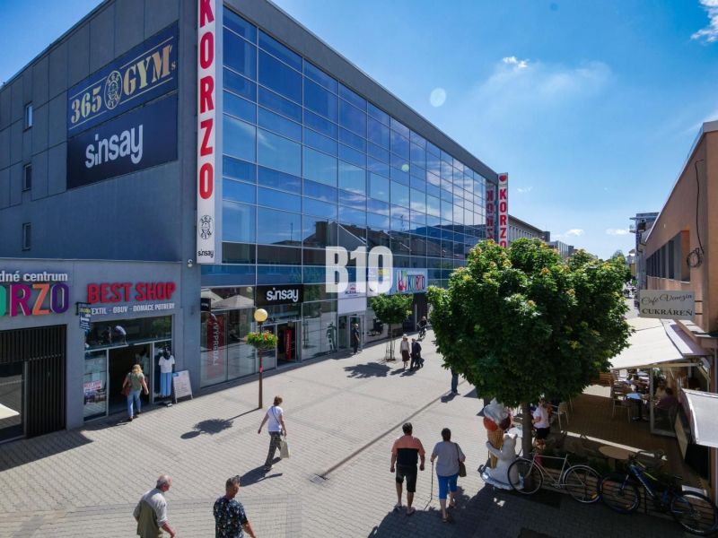 Obchodné priestory s charakterom v srdci Topoľčian – investícia, ktorá - Obchodné priestory na Obchodnej ulici v Topoľčanoch, ľudia prechádzajú popri moderných budovách.