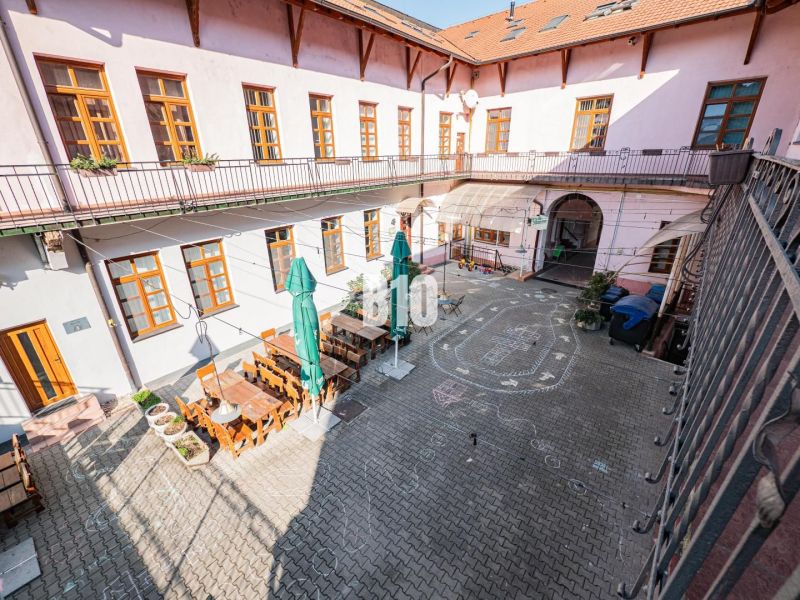 Autentický podnik v Starom Meste - ODSTÚPENIE - Dvor s terasou a stolmi v obchodných priestoroch v Nitre, obklopené historickou architektúrou.