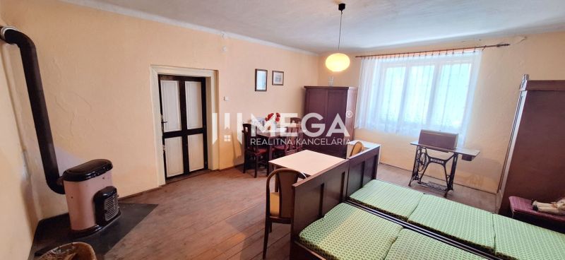 ZNÍŽENÁ CENA -  NA PREDAJ Dom v obci Kochanovce - Izba v rodinnom dome s pecou, stolom a posteľou, podlaha s dreveným dekorom.