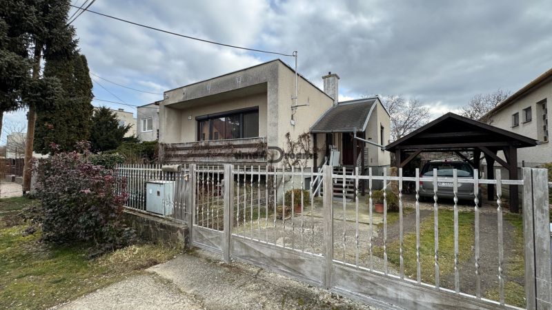 NA PREDAJ rodinný dom v Jelšovciach - EXKLUZÍVNE - Rodinný dom so záhradou, oplotením, dreveným prístreškom a bránou, v pochmúrnom počasí.