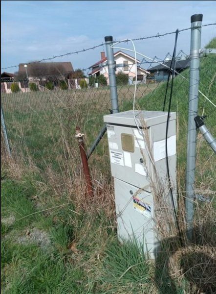 Pozemok v Dunajskej Lužnej  - Plot s trávou a elektrickým rozvádzačom na pozemku na bývanie v Dunajskej Lužnej.