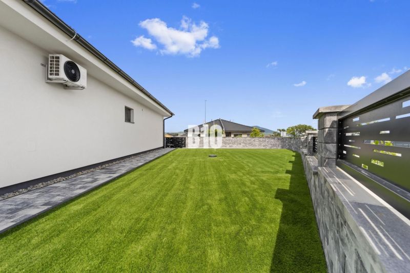 Moderný 4i dom v RED OAK, Lužianky | Kompletné zariadenie! - Záhrada rodinného domu v Nitre s trávnikom a kamennou dlažbou pri stene.