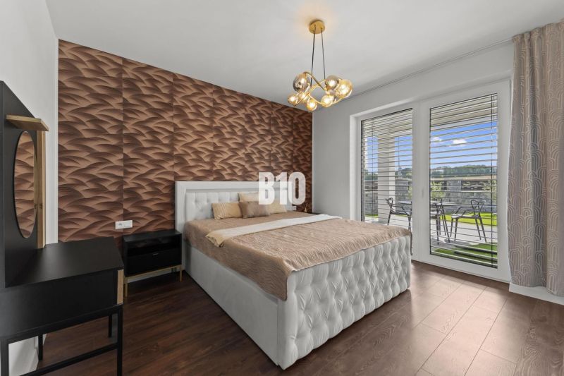 Moderný 4i dom v RED OAK, Lužianky | Kompletné zariadenie! - Spálňa s podlahou s dreveným dekorom, prešívaným posteľným čelom a výhľadom na terasu.