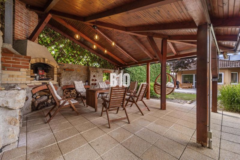 4i rodinný dom Lehota | 230 m² | Bazén | 85 m² garáž | 5 min. od Nitry - Zastrešená terasa s krbom a drevenými stoličkami pri rodinnom dome v Nitre.