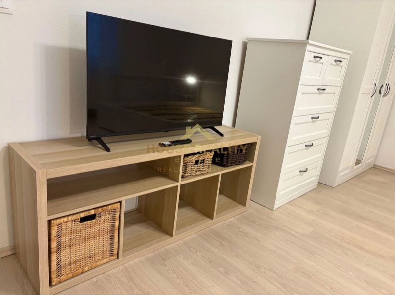 Pekný prenájom 1 izbový byt, Trenčianska ulica, Bratislava II Ružinov  - TV na poličke s košíkmi, vedľa komody a skrine, podlaha s dreveným dekorom.