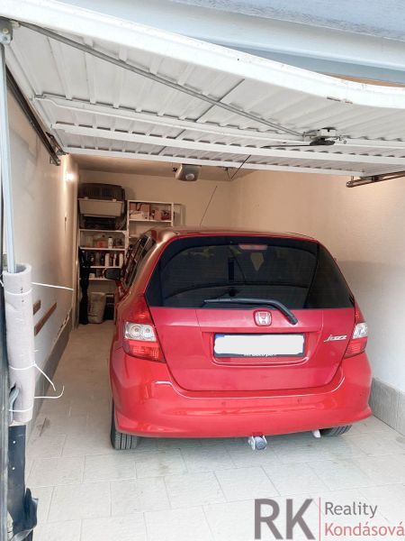 Garáž na prenájom- Staré mesto- Belanská, automatická brána - Červené auto zaparkované v garáži s regálmi na stene, podlaha z dlažby.
