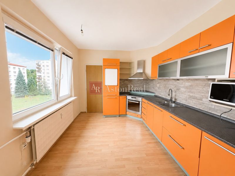 Predaj! slnečný 3-izbový byt s loggiou 74 m² Podbreziny - LM - Kuchyňa v 3-izbovom byte s oranžovými skrinkami a podlahou s dreveným dekorom.