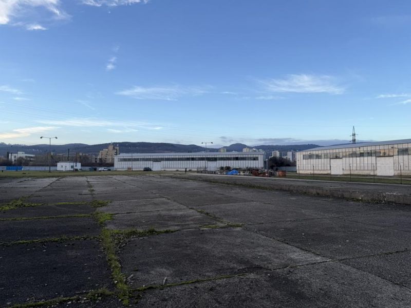 Sklad. priestory 200m2 - 1000m2, spevnené plochy do 6000m2 v areáli. - Exteriér skladov a hál v Bratislave - Rači so spevnenou plochou a horami v pozadí.