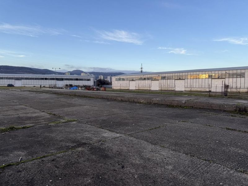 Sklad. priestory 200m2 - 1000m2, spevnené plochy do 6000m2 v areáli. - Sklady a haly v Bratislave - Rači, priemyselná zóna s budovami a asfaltovou plochou.