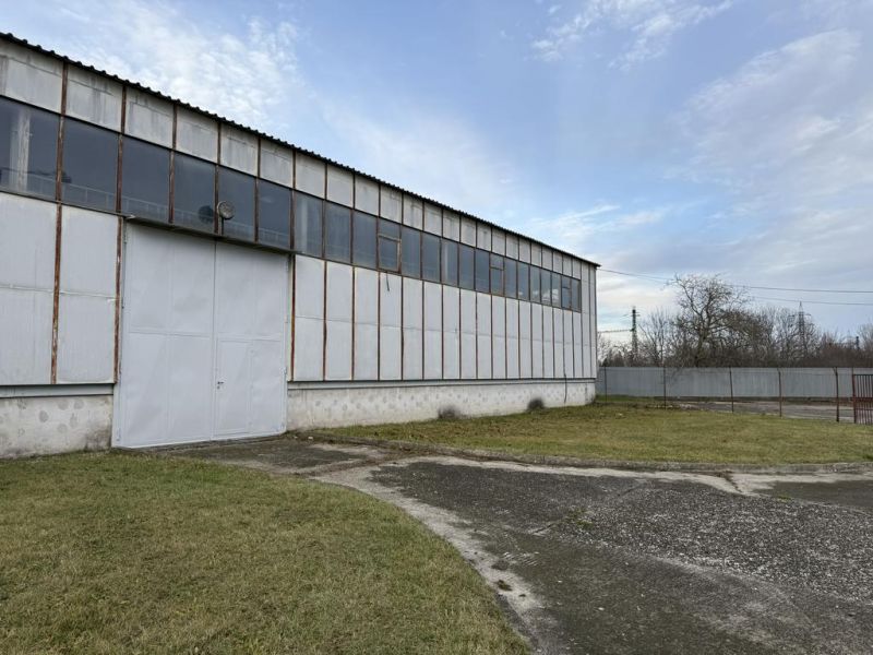 Sklad. priestory 200m2 - 1000m2, spevnené plochy do 6000m2 v areáli. - Skladová hala v Bratislave-Rači s oceľovou konštrukciou a zeleným trávnikom v popredí.